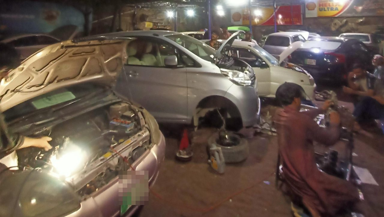 Mechanics working on cars with open bonnets in the Safdar Auto Workshop bays in the evening