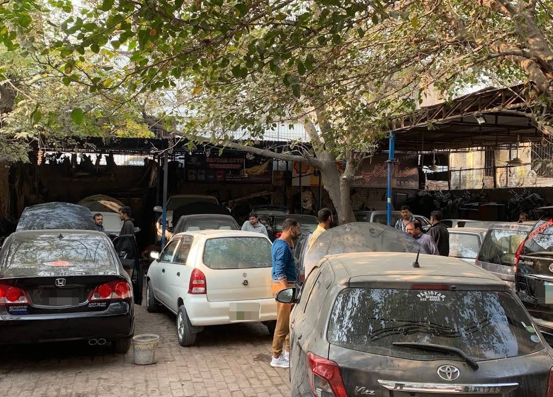 Mechanics and customers around cars in the Safdar Auto Workshop yard